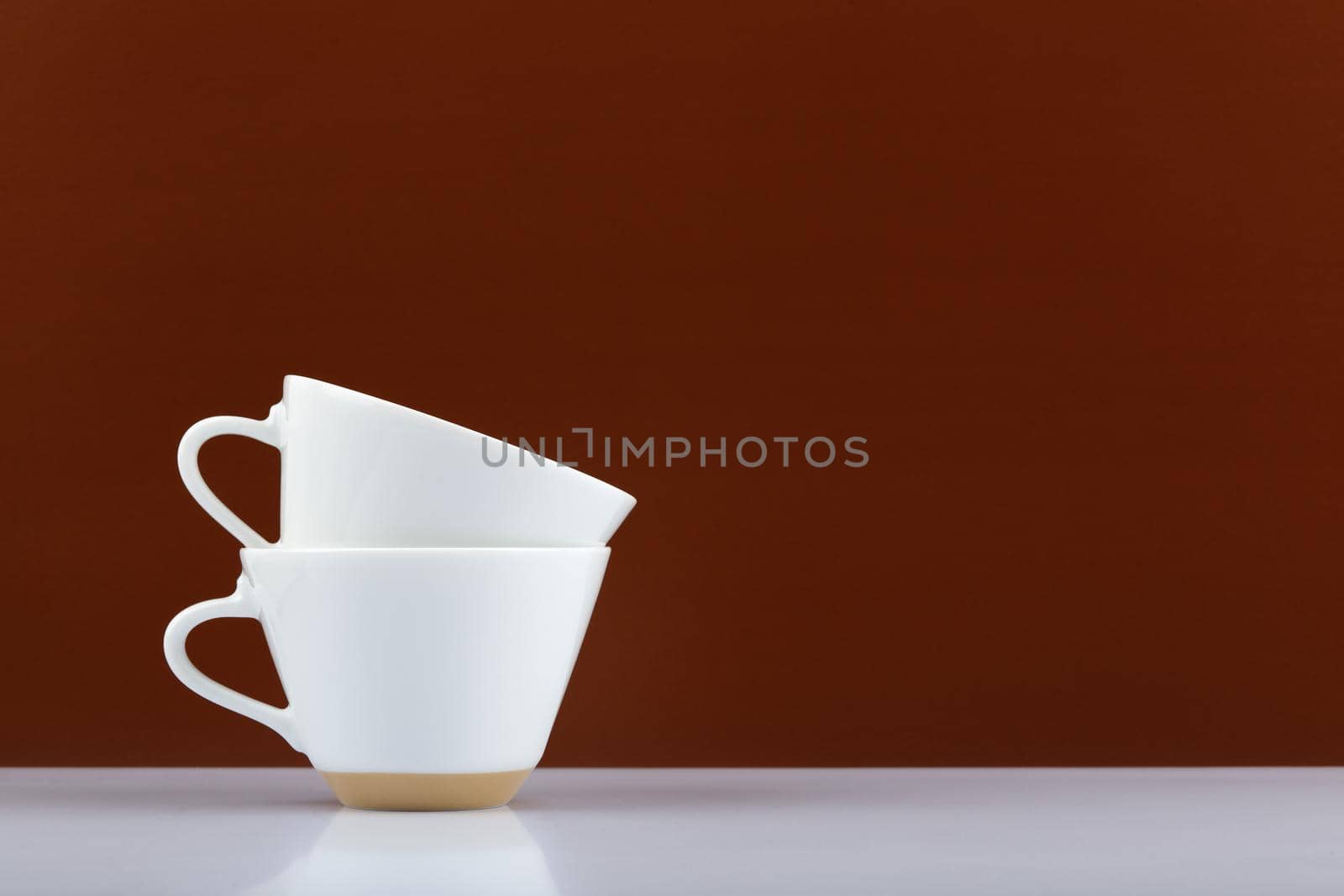 Two white coffee cups on in another on white table against brown background with copy space by Senorina_Irina