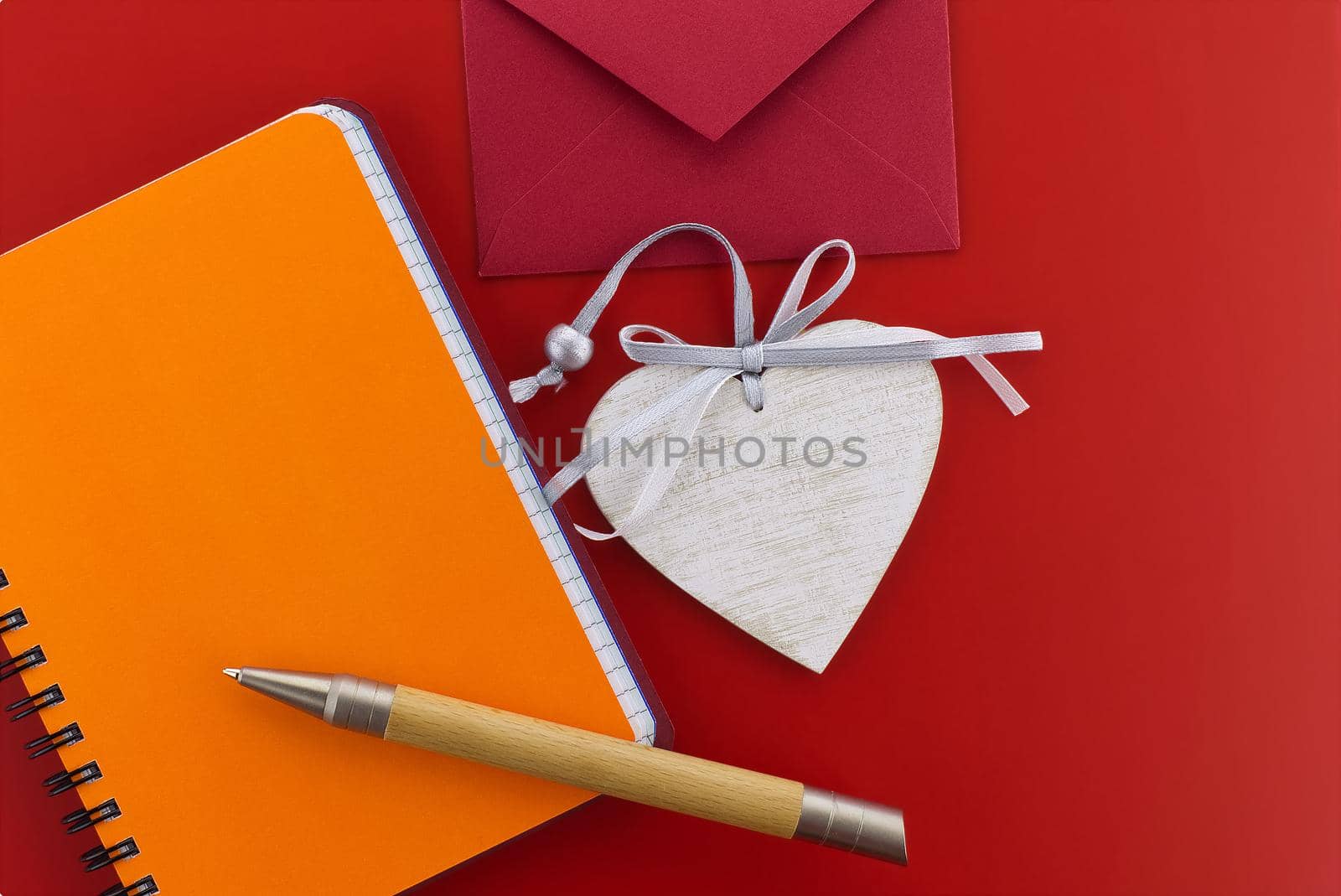 Heart medallion, wire bound notepad, pen and envelope on red background. Greetings and love letter