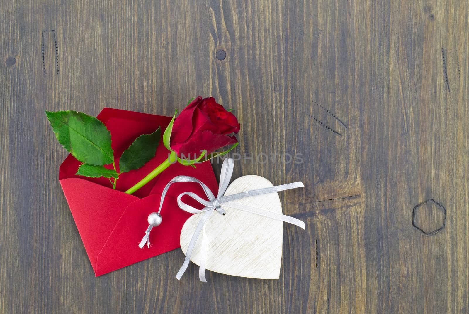 Red rose in envelope and heart medallion on wooden background with free copy space. Wishes, greetings and love message
