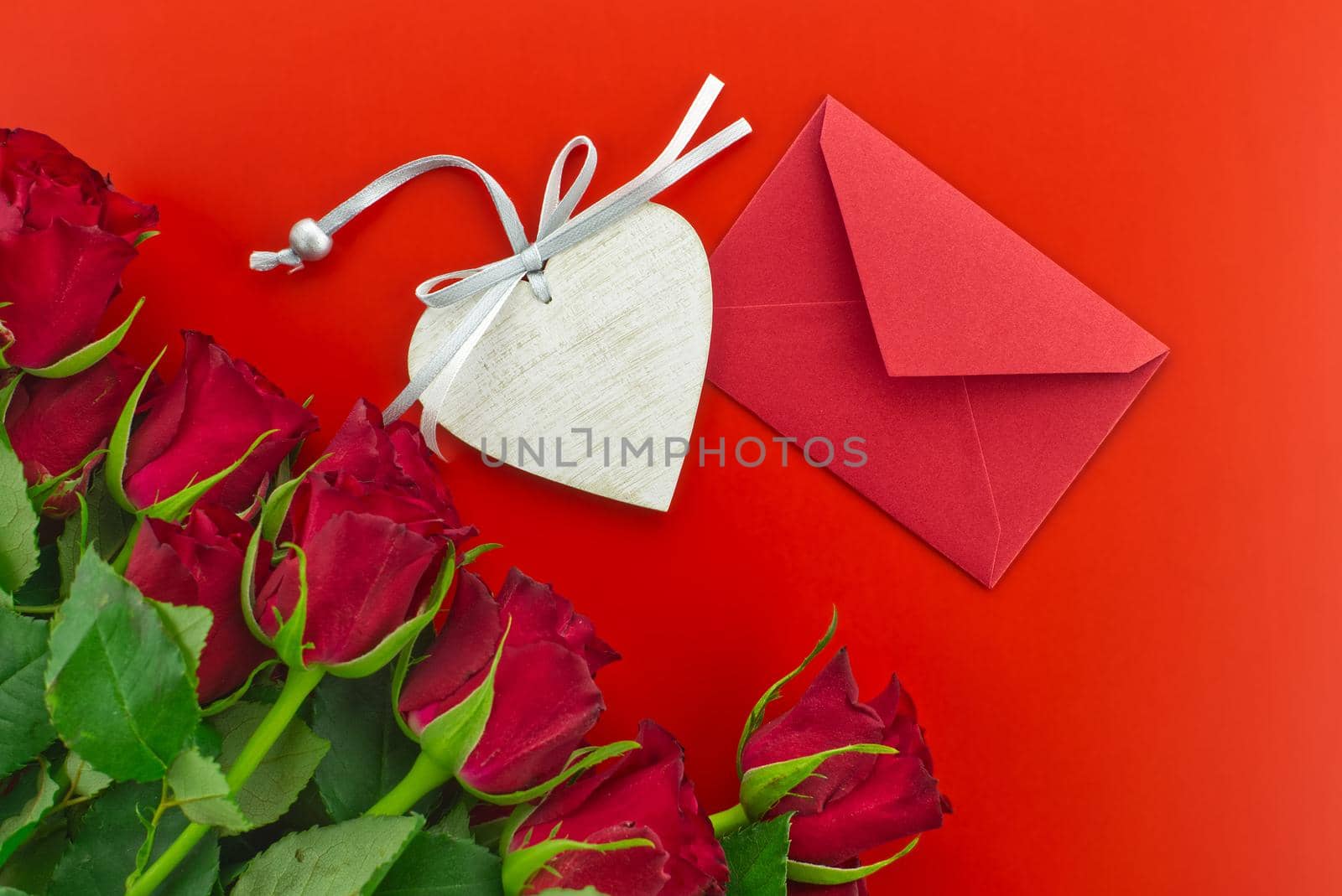 Red roses, envelope and wooden heart medallion on red background with free copy space. Wishes, greetings and love message