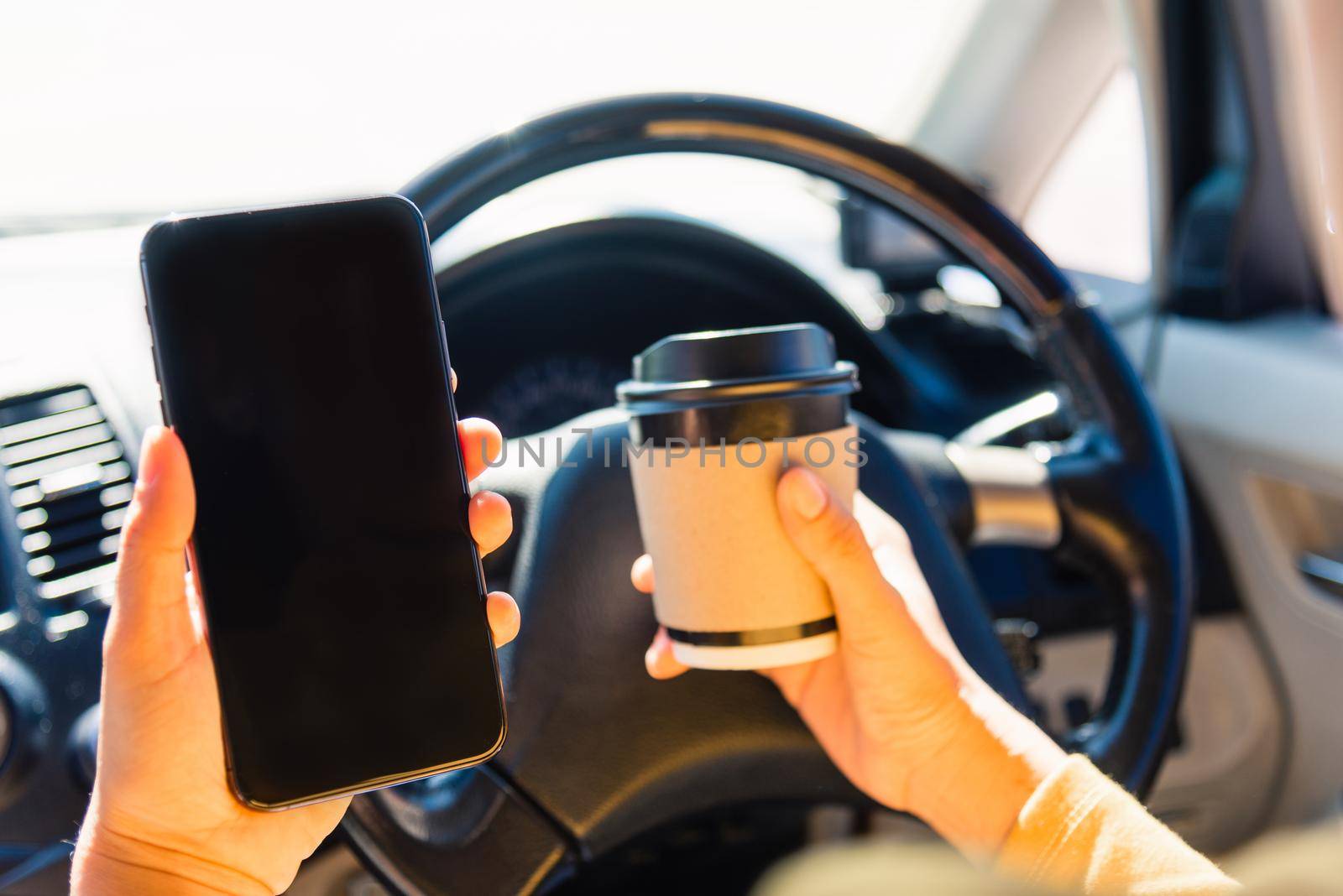 woman drinking hot coffee takeaway cup inside a car and using smartphone by Sorapop