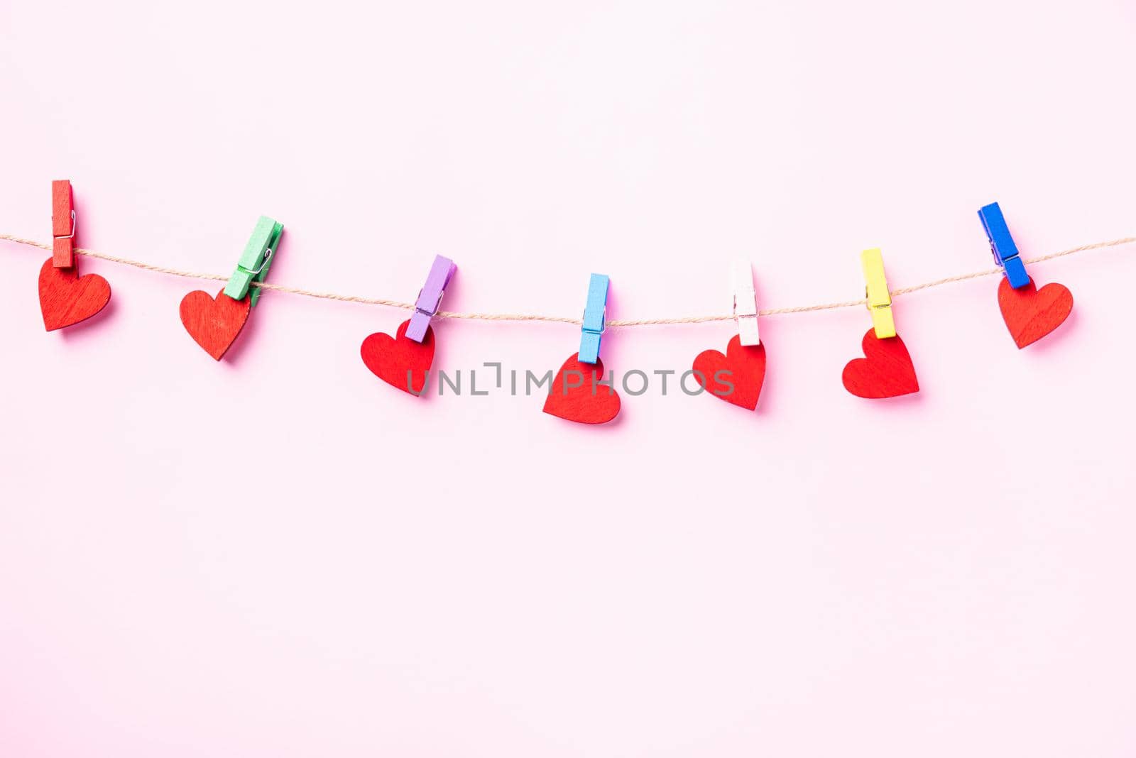Happy Valentine's day concept. red heart-shaped valentines decoration hanging with wood clips for love on the rope isolated on pink background with copy space