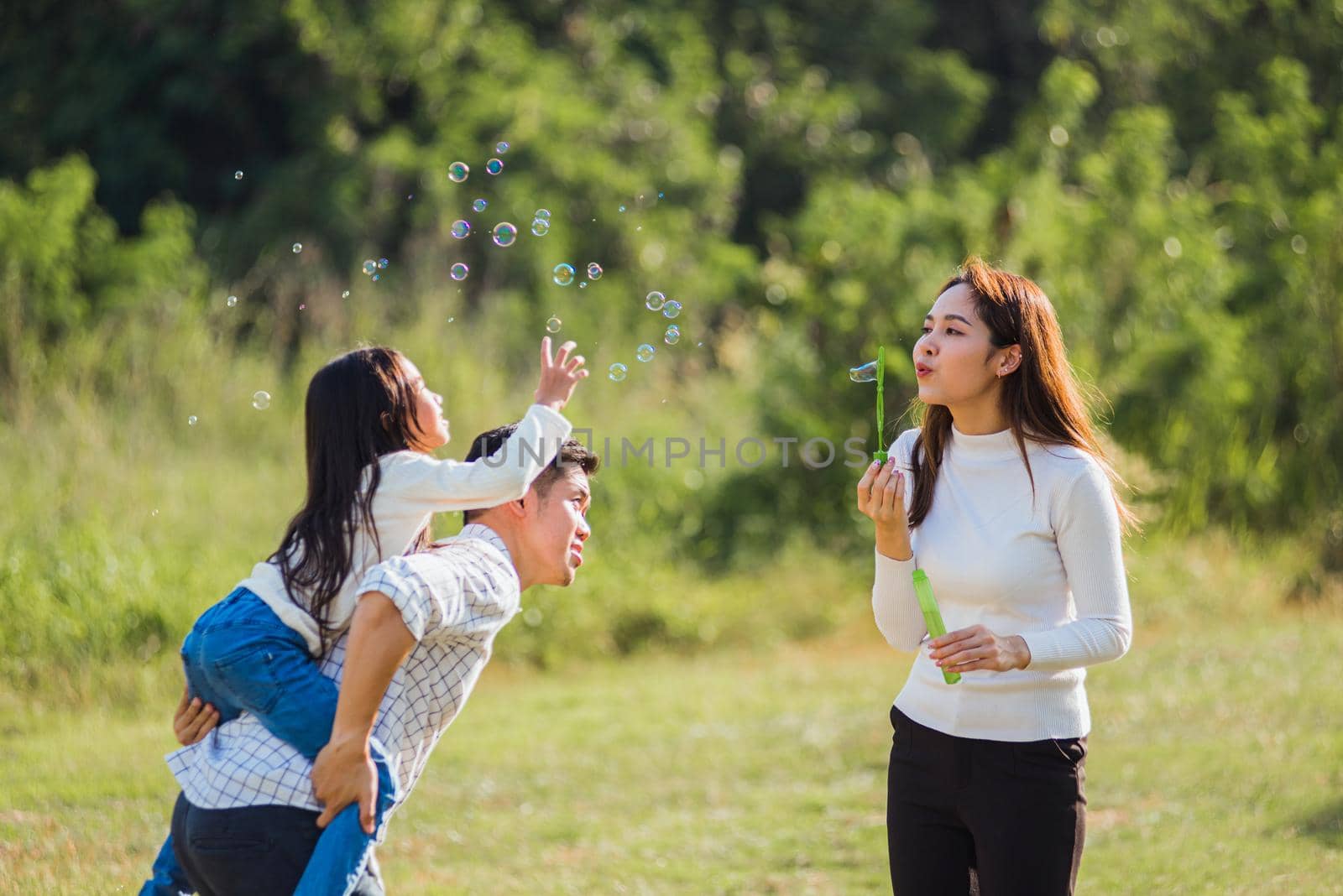 Asian family mother, father and little girl having fun together play blowing soap bubbles in park by Sorapop