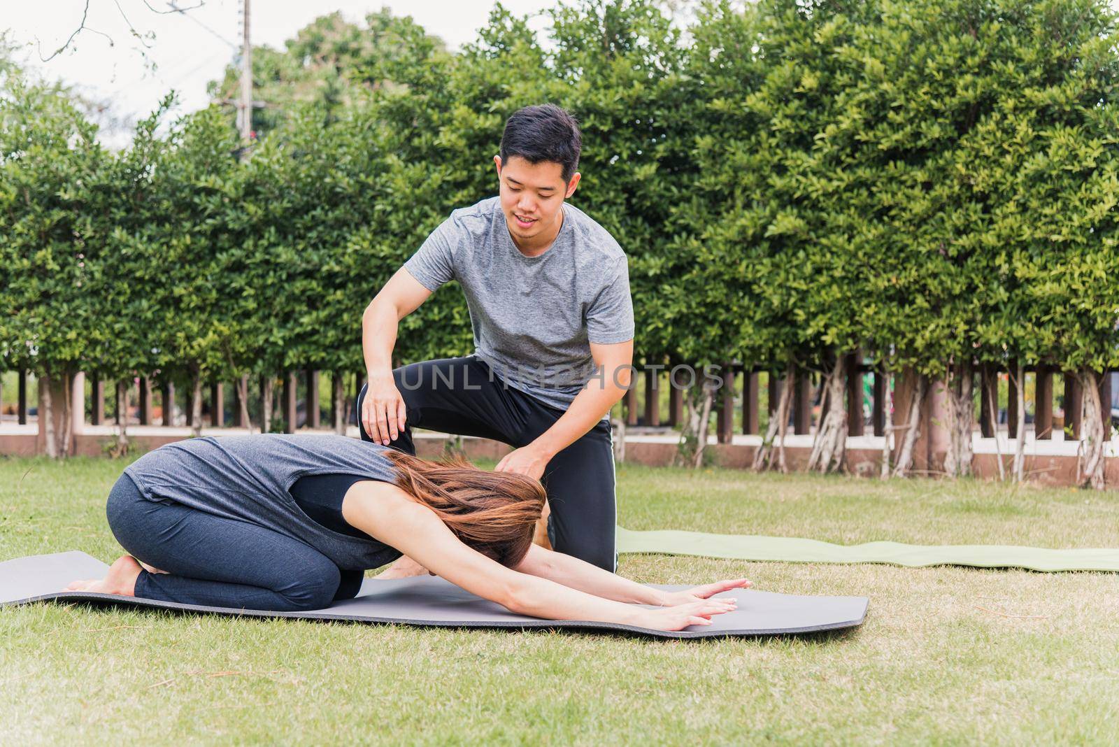 Asian man and woman training yoga outdoors in meditate pose sitting on green grass. Young couple practicing doing stretching in nature a field garden park together. Meditation health care concept