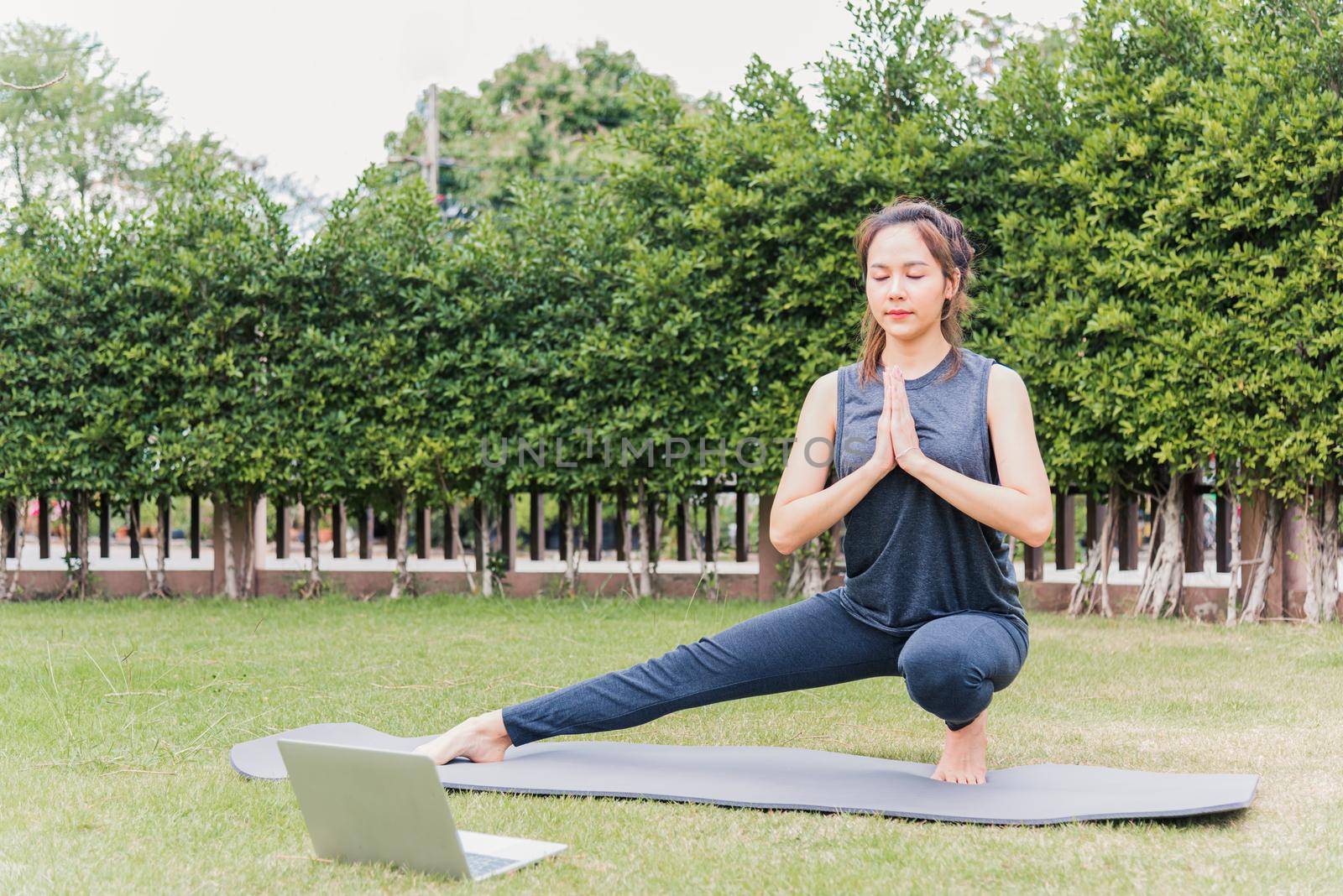 woman using laptop during online video training practicing yoga outdoors by Sorapop