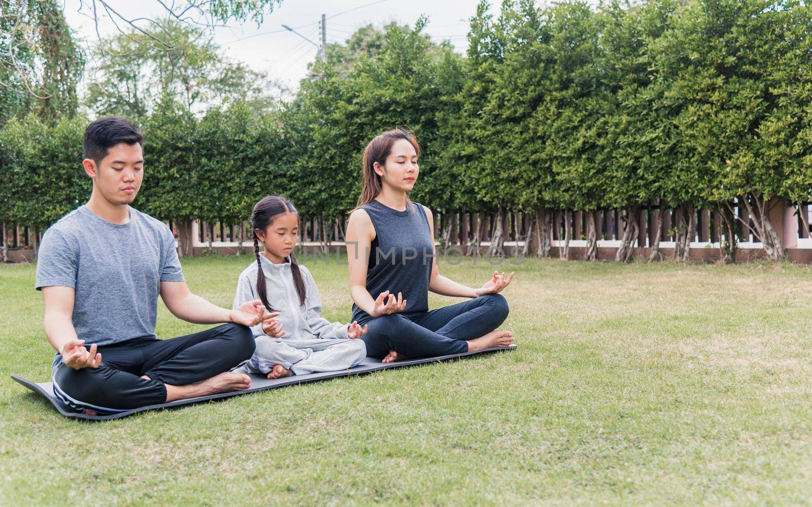 mother, father practicing doing yoga exercises with child daughter outdoors in meditate pose together by Sorapop
