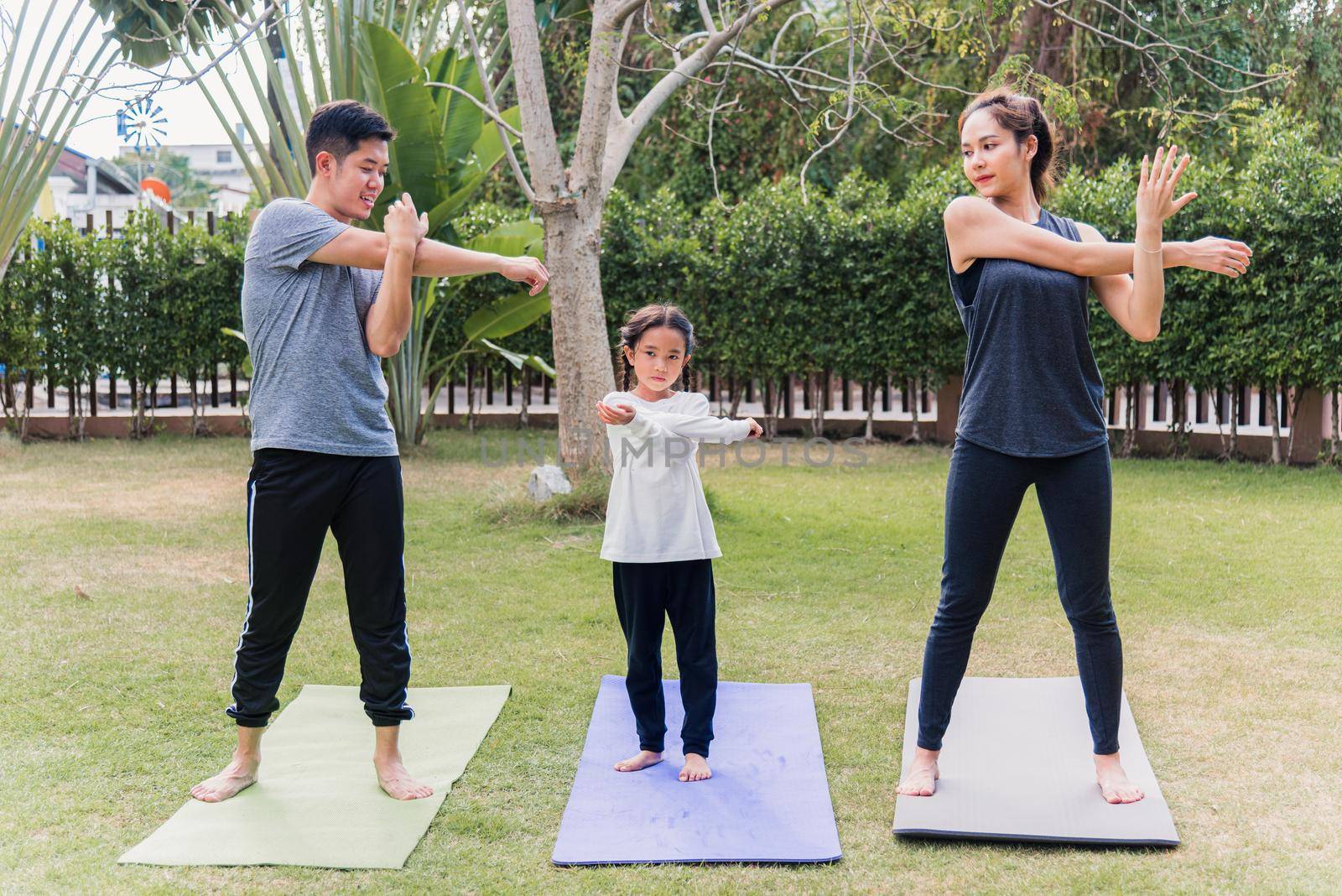 Asian young mother, father and child daughter practicing exercising stretching together before yoga workout outdoor morning in nature a field garden park. Happy family kid sport healthy lifestyle