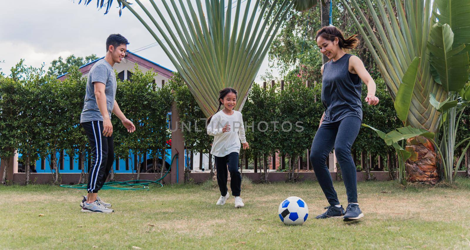 mother, father and child daughter playing soccer outside in nature a field garden park by Sorapop