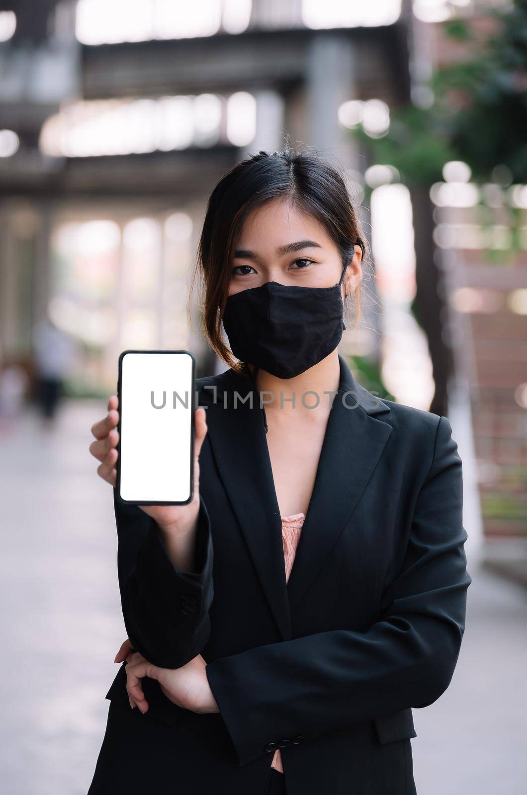 Portrait Of Attractive Asian Businesswoman wear mask during show mobile phone display with white screen by nateemee