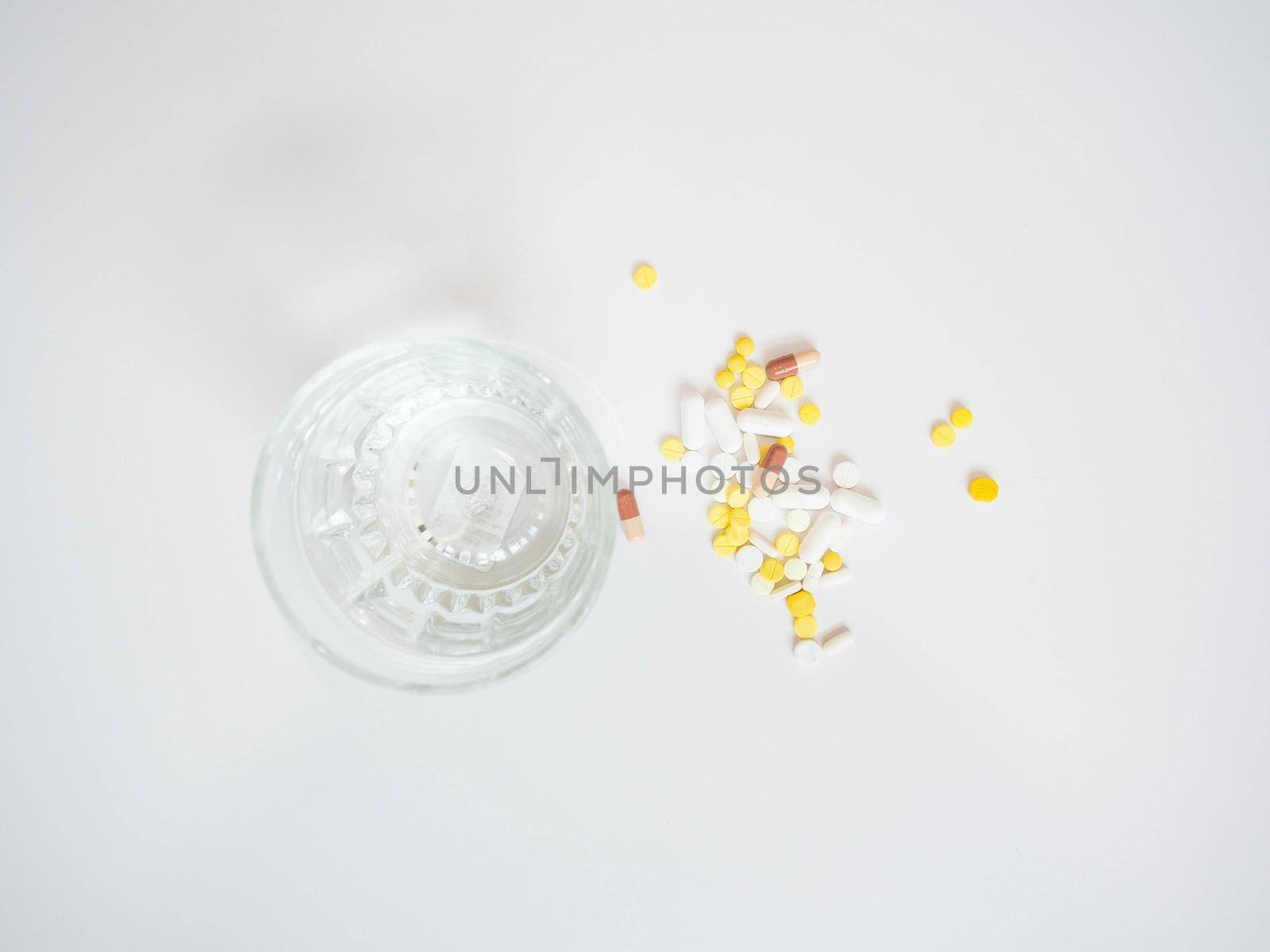 Multi colored pills with a glass of water placed on a white background