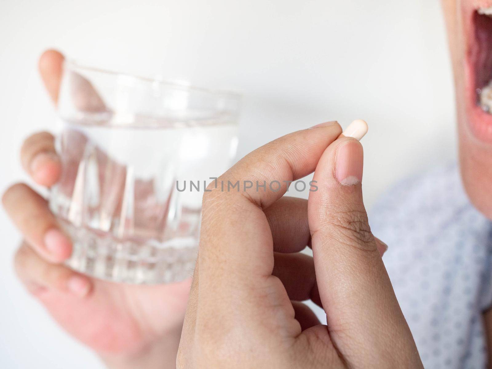 A woman taking a pill into her mouth The other A woman taking a pill into her mouth The other hand holds water. holds water.