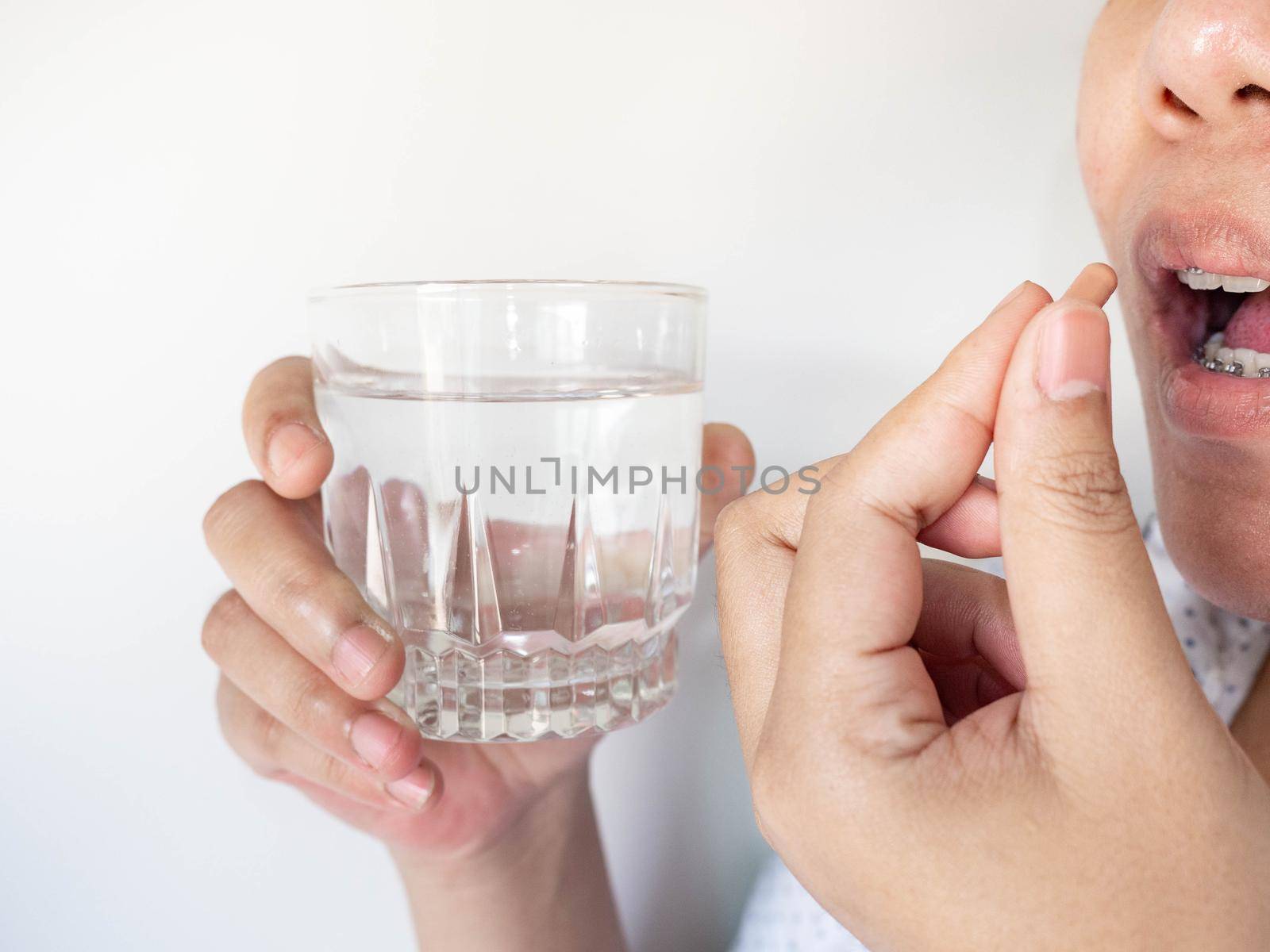 A woman taking a pill into her mouth The other A woman taking a pill into her mouth The other hand holds water. holds water. by Kulpreya