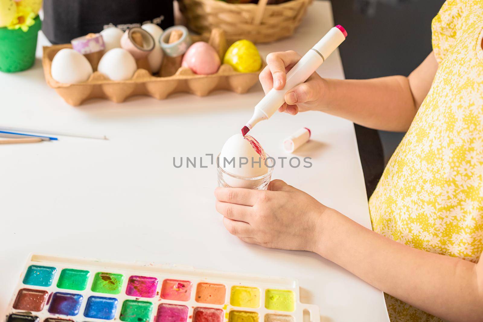 Close-up partial view of little child painting easter egg at table.