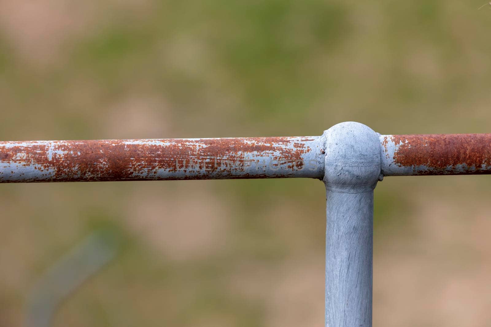 A rusty steel galvanised fence post and hand rail on a green grass background