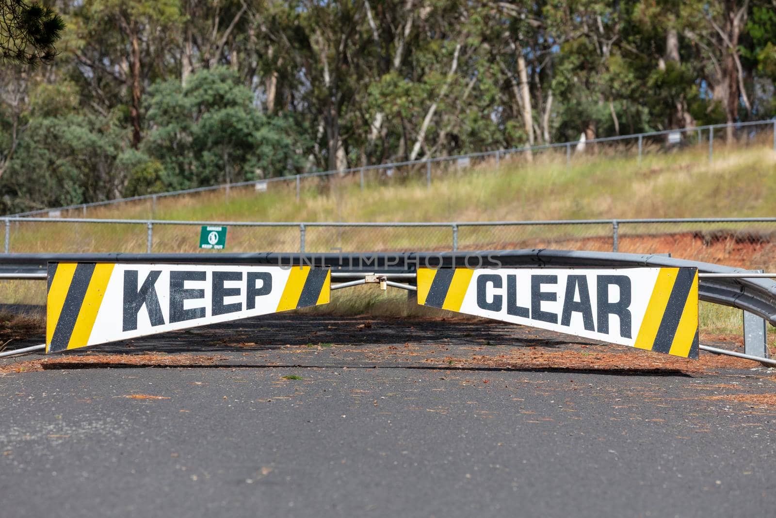 A safety keep clear boom gate on a road near bushland and a steel fence