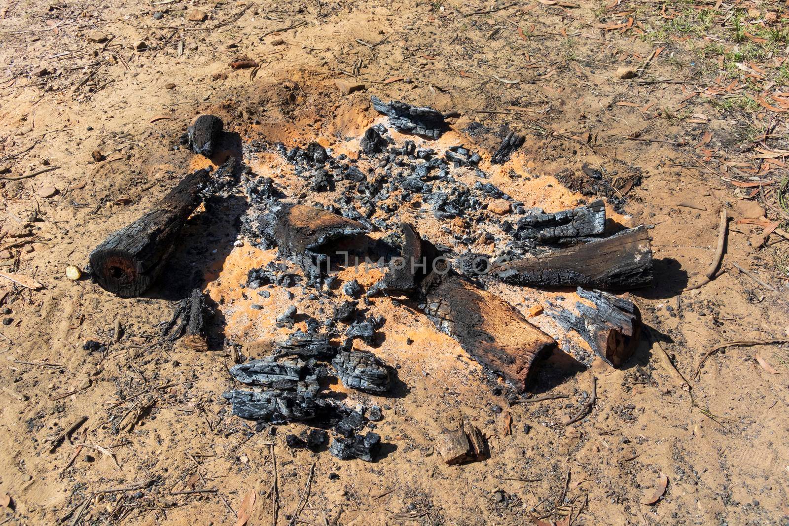 Burnt wood and coals from a recent campfire on brown dirt in The Blue Mountains in regional New South Wales in Australia