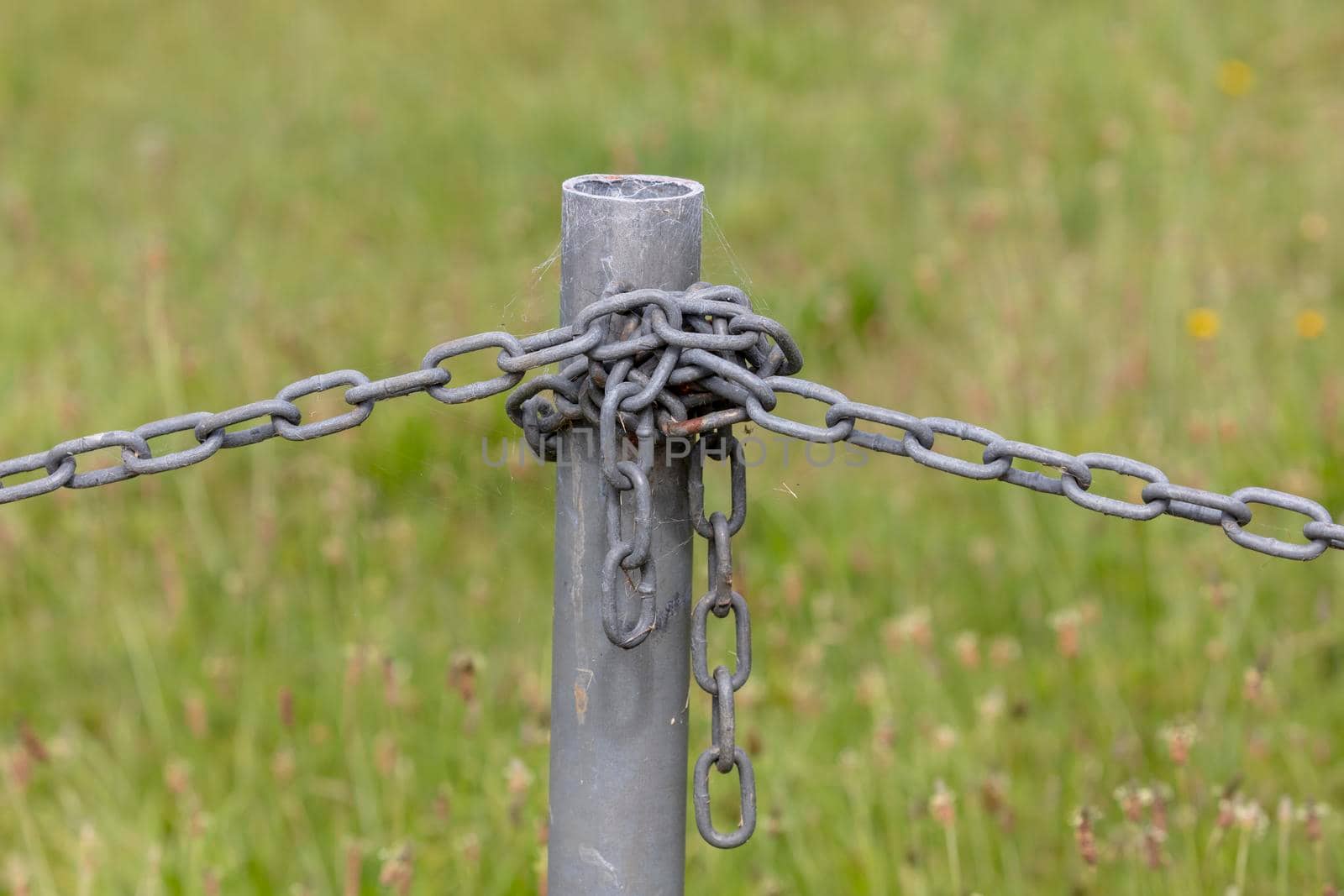 Industrial chain attached to a galvanised fence post in a green field