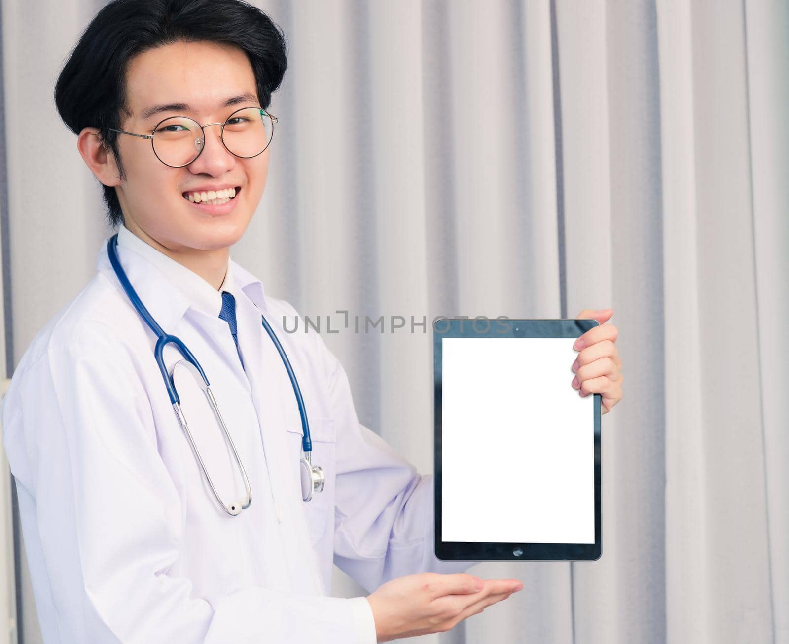 Doctor in uniform and stethoscope neck strap showing front blank screen smart digital tablet on hand by Sorapop