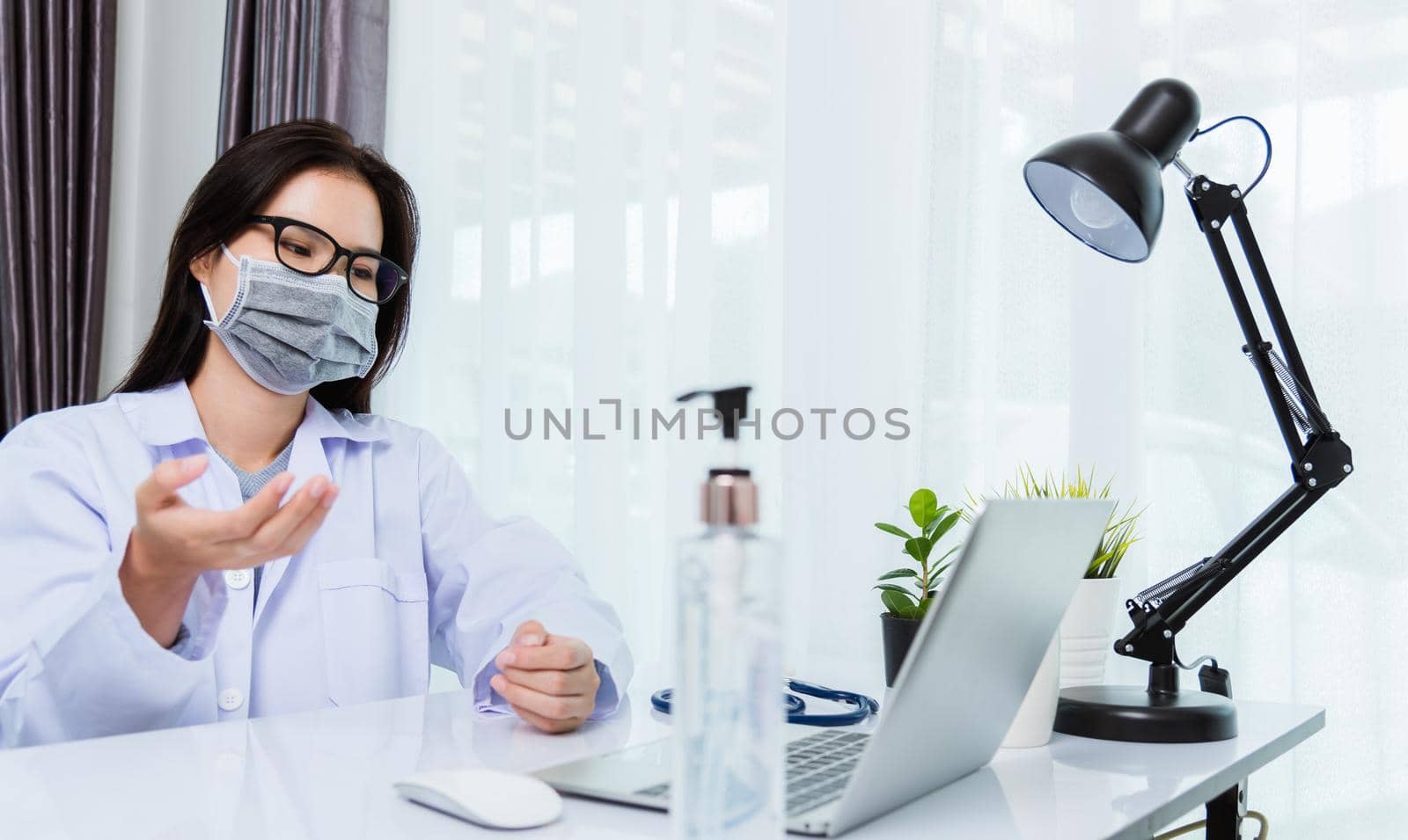 Asian young beautiful woman doctor wear face mask protective video call conference online raise hand explain to patients on laptop computer quarantines disease coronavirus or COVID-19 at hospital