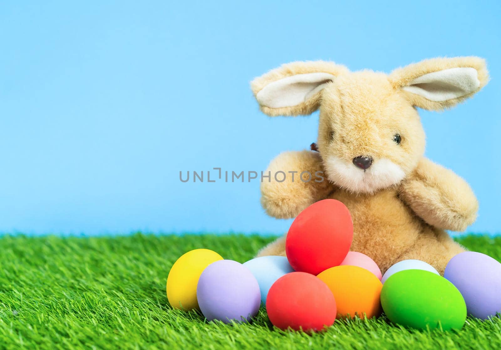 Colorful easter eggs and bunny on grass with blue background