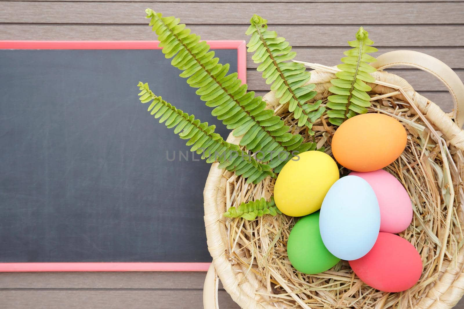 Colorful easter eggs in the basket and blackboard on wood background with space