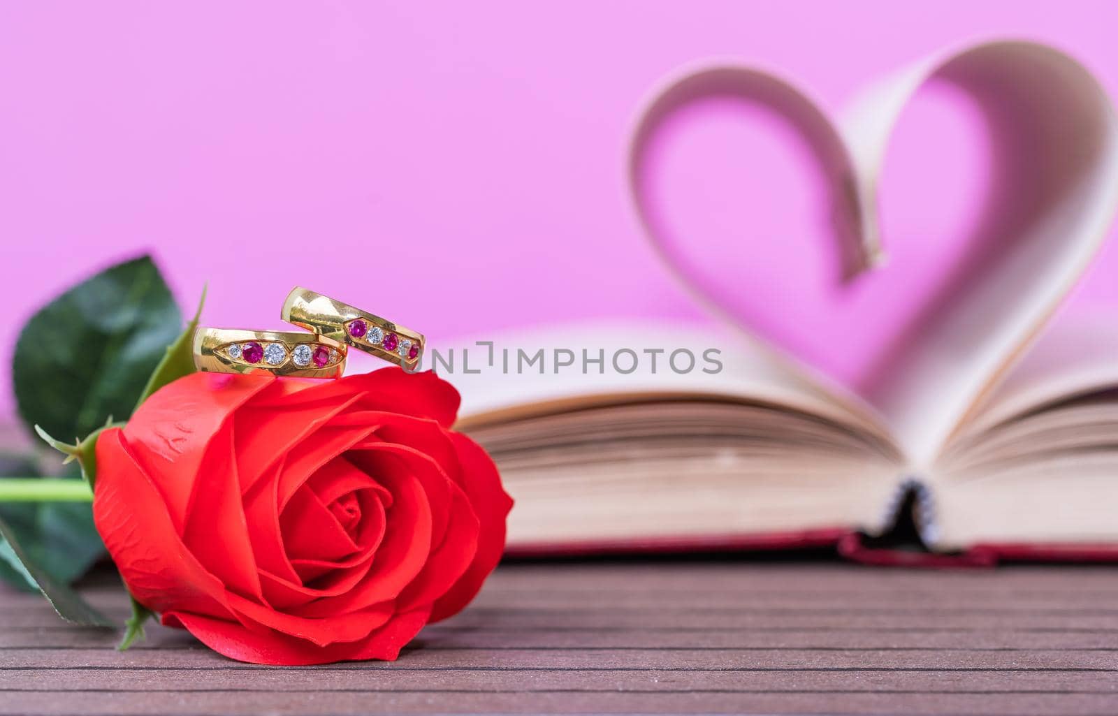 Pages of book curved into a heart shape and red rose. Love concept of heart shape from book pages on pink background