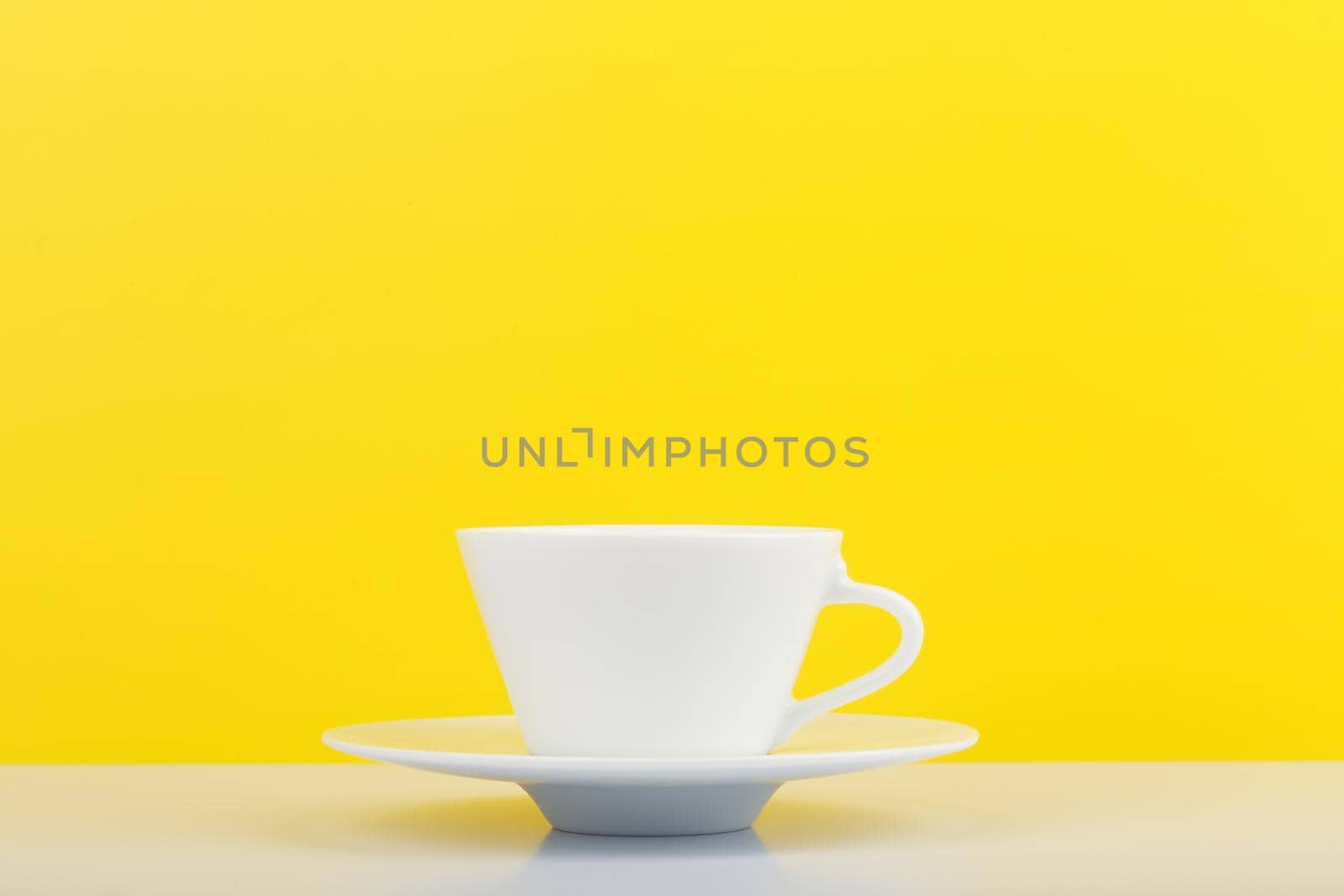 Minimalistic still life with white glossy cup of coffee on white table against yellow background with copy space. High quality photo