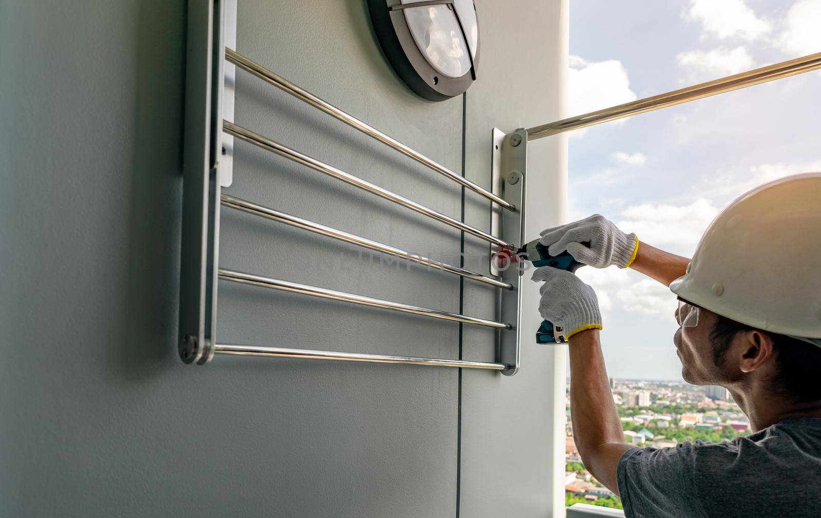 Asian man screwing screw install clothesline with cordless drill. Technician wears safety helmet and hand holding drilling tool for apartment renovation. Man working home improvement with DIY concept. by Fahroni