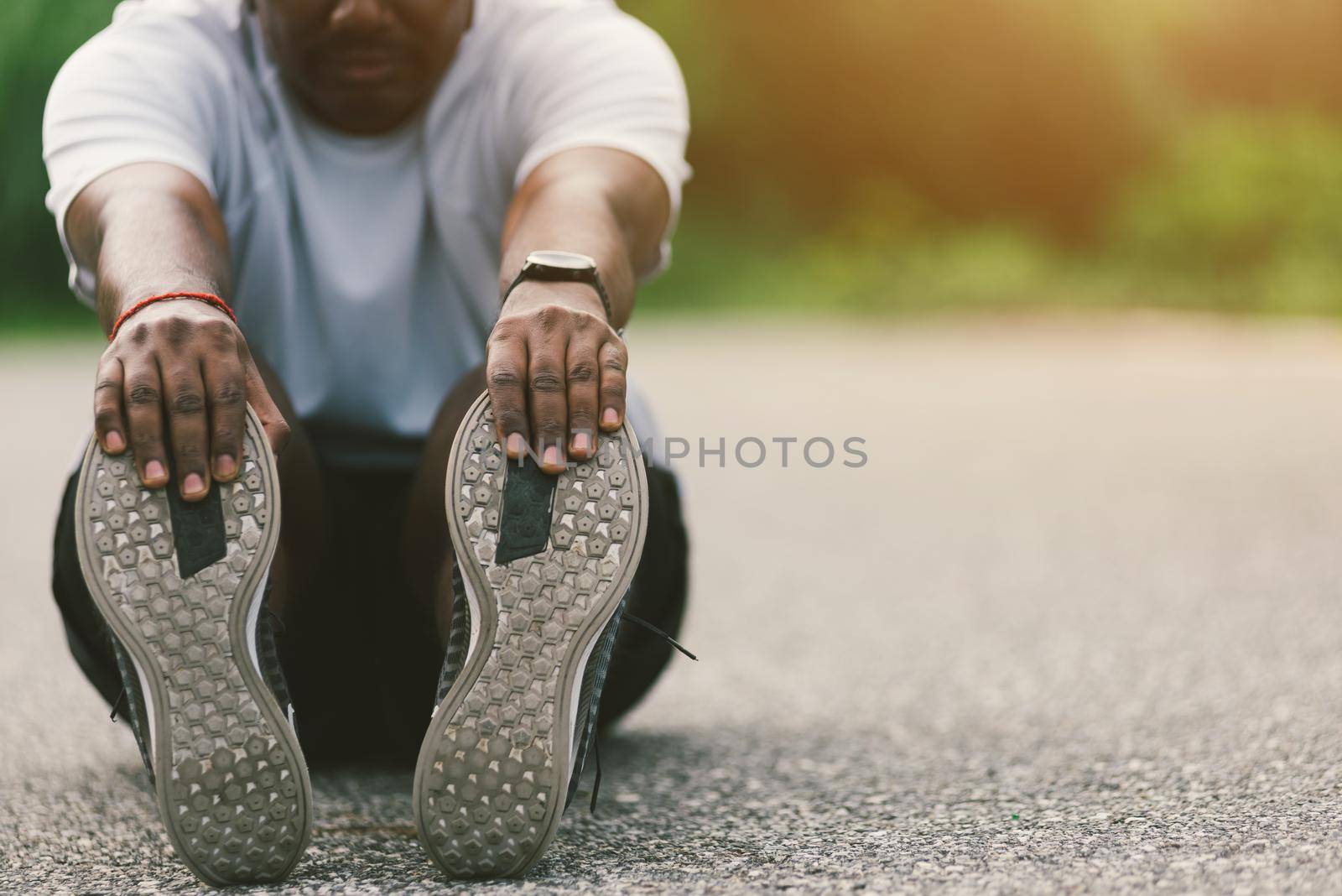 sport runner black man wear watch he sitting pull toe feet stretching legs and knee by Sorapop