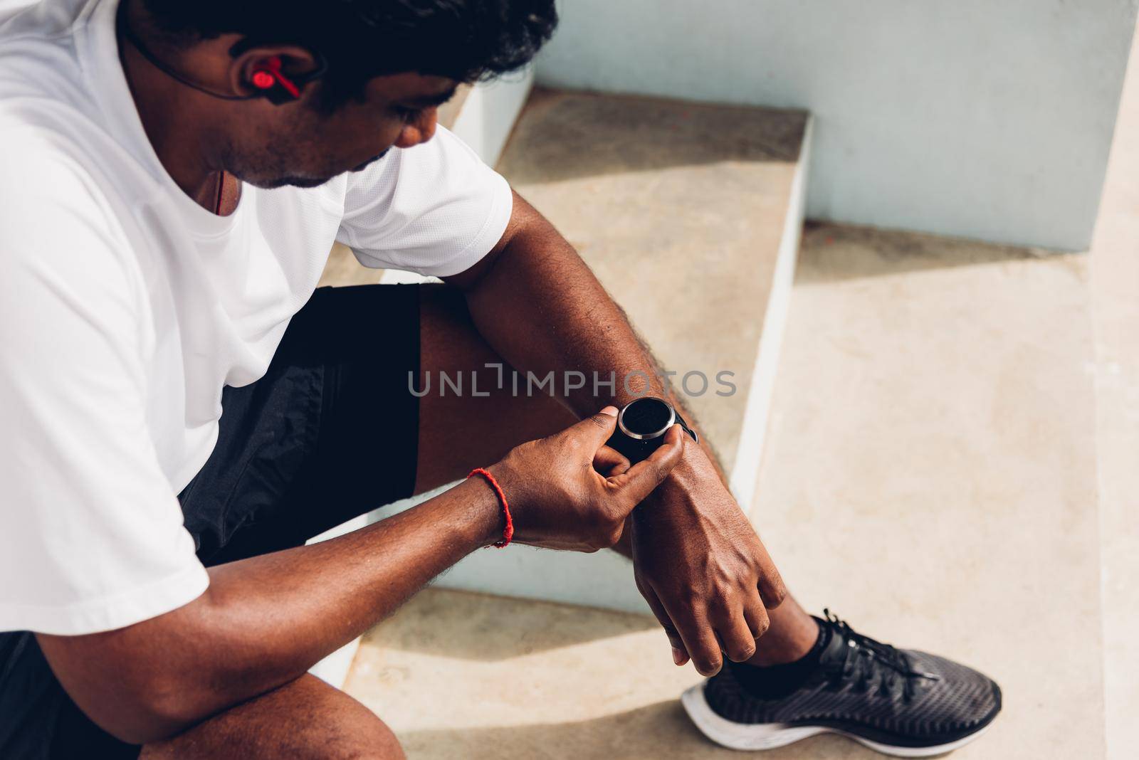 Close up Asian young athlete sport runner black man wear modern time smart watch he sitting resting before training running at the outdoor street health park, healthy exercise before workout concept