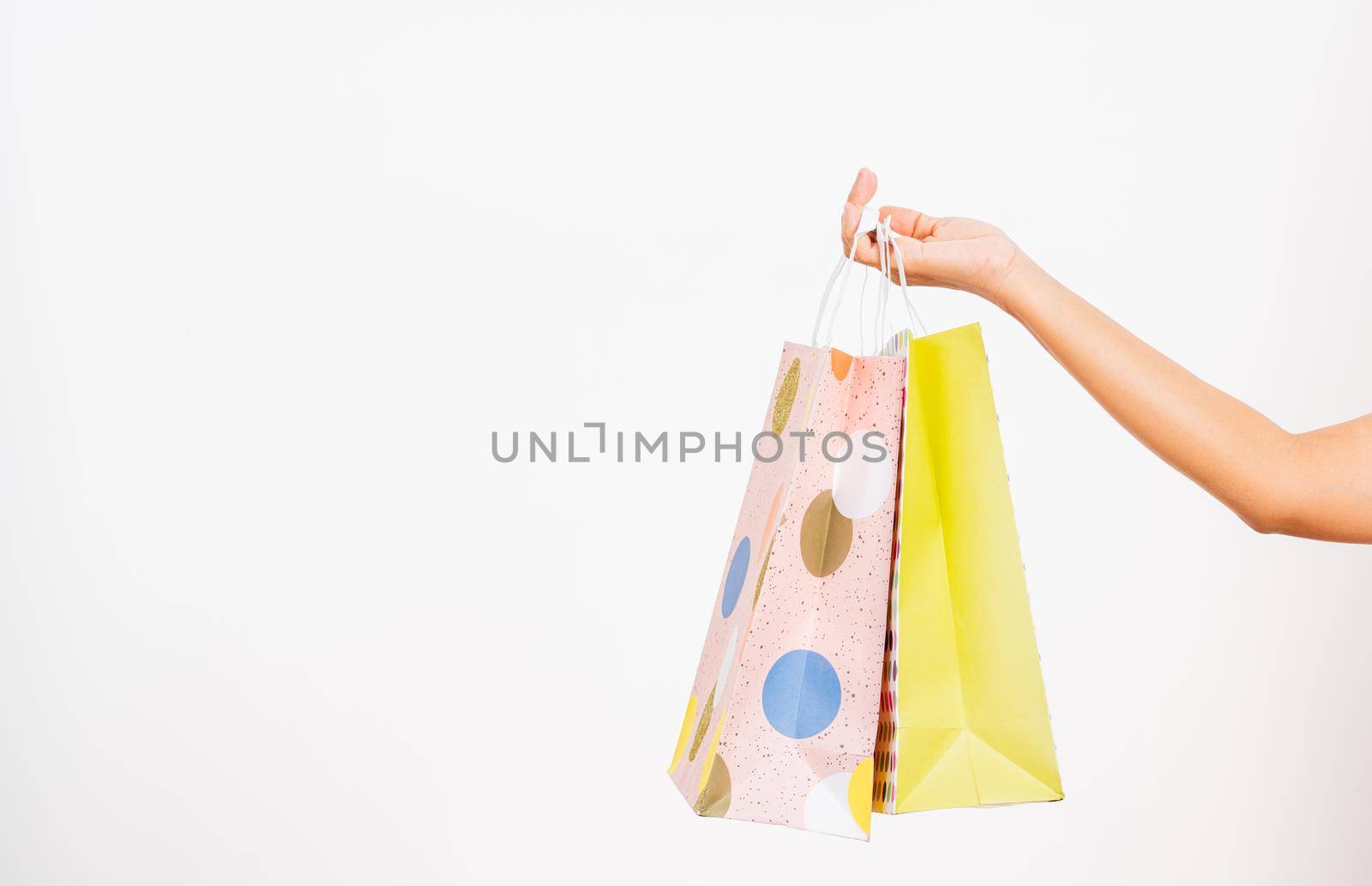 Closeup women hand holding colorful multicolor shopping bag many packets isolated on white background, female holds in hand white clear empty blank craft paper gift bag, shopping day concept