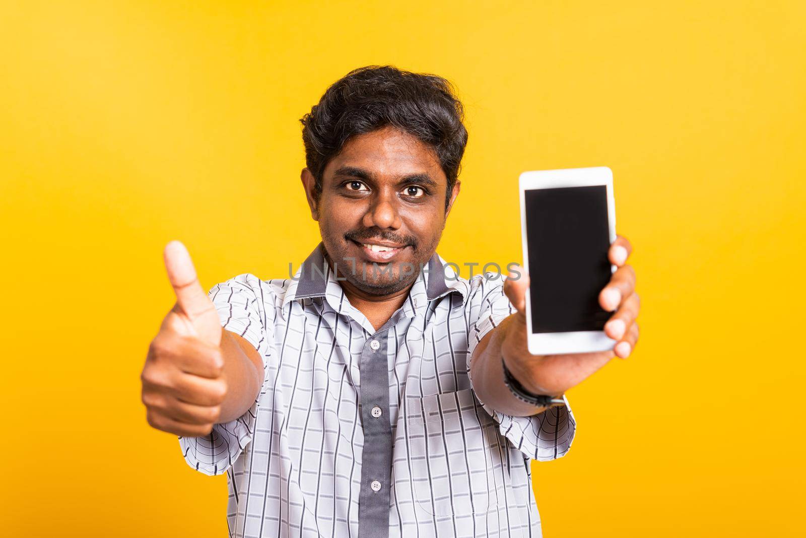 Closeup Asian happy portrait young black man smile showing a mobile smartphone blank screen and finger thumb up for a good sign, studio isolated on yellow background