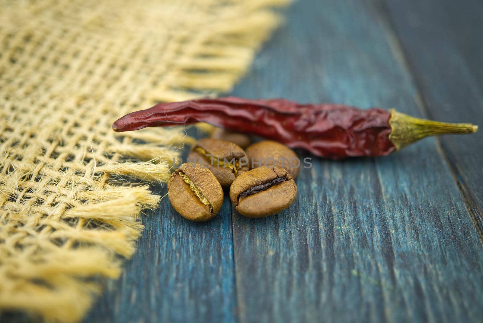 Macro photo of dried red chili pepper and roasted coffee beans on wooden and hessian or burlap fabric background