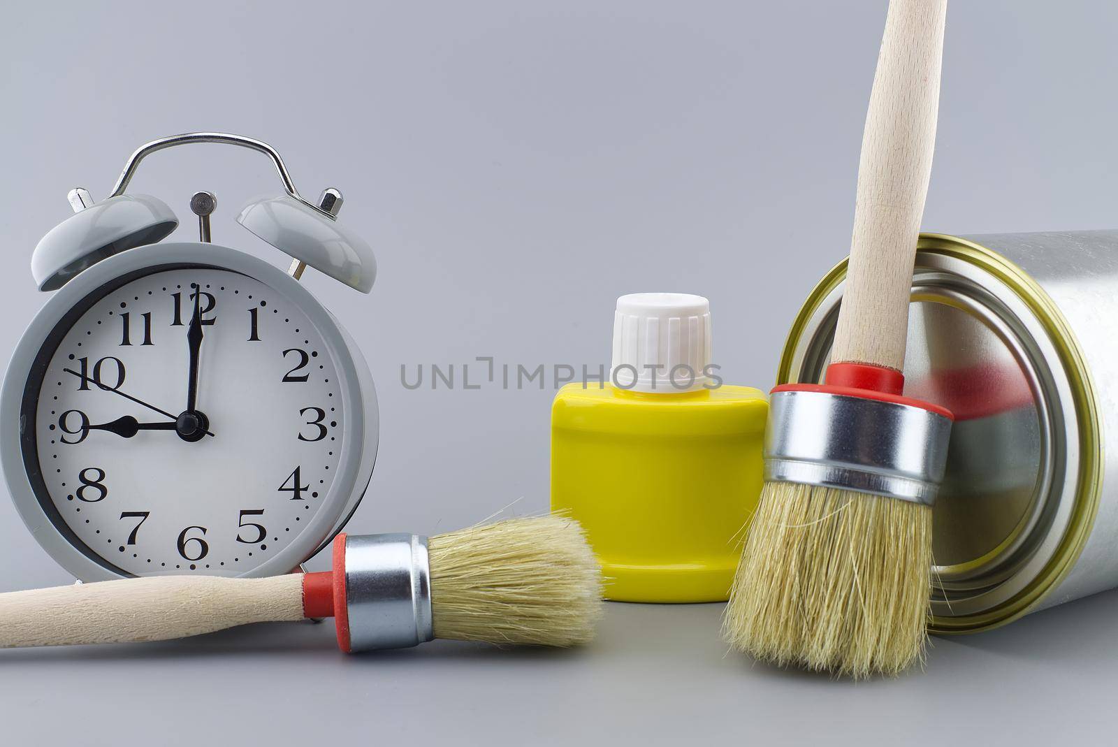 New color, decorating or renovations concept with a still life of an alarm clock with assorted clean paint brushes and unlabeled tin of paint over a grey background