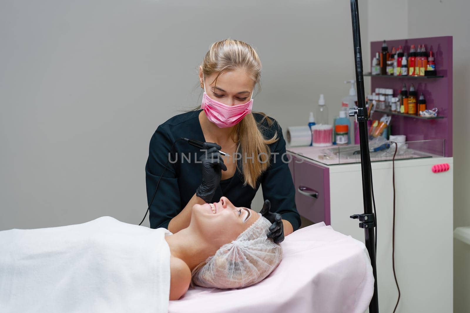 Cosmetology cabinet client lies on couch. Beautician applies permanent ink on eyebrows. Procedure of permanent eyebrow makeup. Free space. Beauty industry