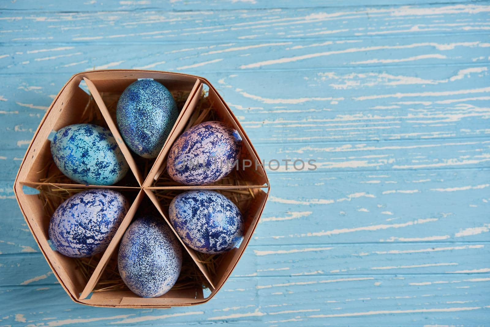 Blue chicken eggs lie in round wooden basket which stands on a blue wooden table. Easter background. Seasonal holiday flat lay with free space for text. Classic blue color of the year 2020