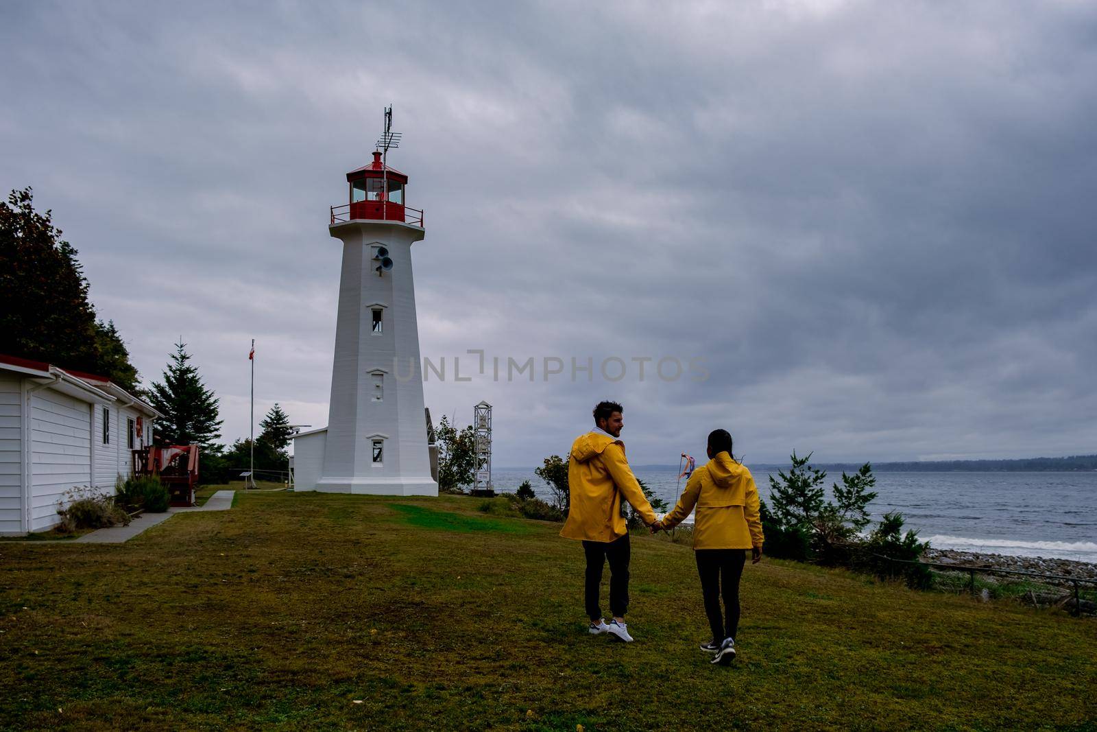 Vancouver Island, Canada, Quadra Island old historical lighthouse at Cape Mudge couple in yellow rain coat during storm by the coast by fokkebok