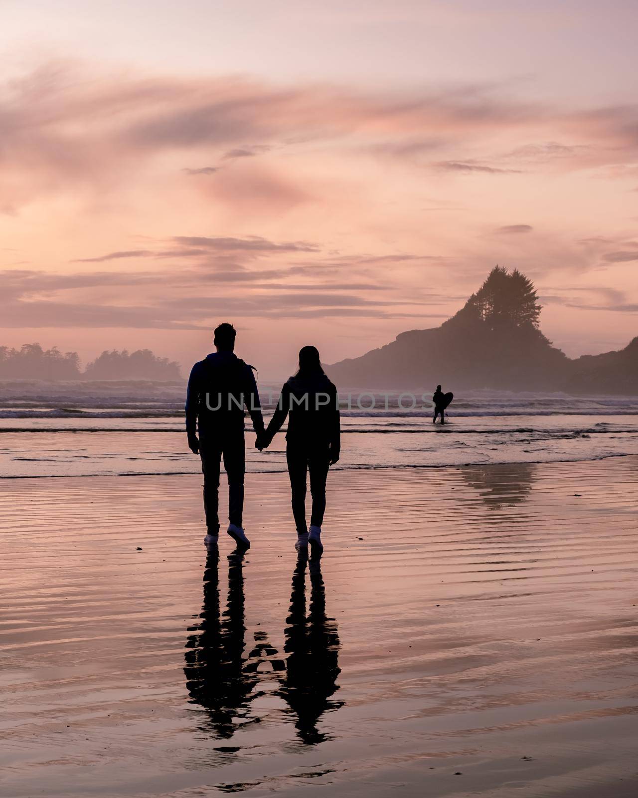 couple of men and women mid-age watching the sunset on the beach of Tofino Vancouver Island Canada, beautiful sunset on the beach with pink-purple colors in the sky. Canada Tofino