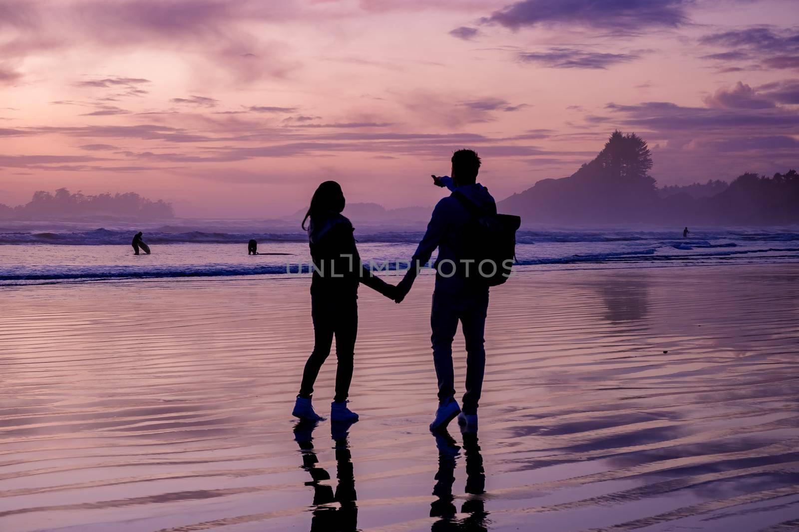 couple men and woman mid age watching sunset on the beach of Tofino Vancouver Island Canada, beautiful sunset on the beach with pink purple colors in the sky by fokkebok