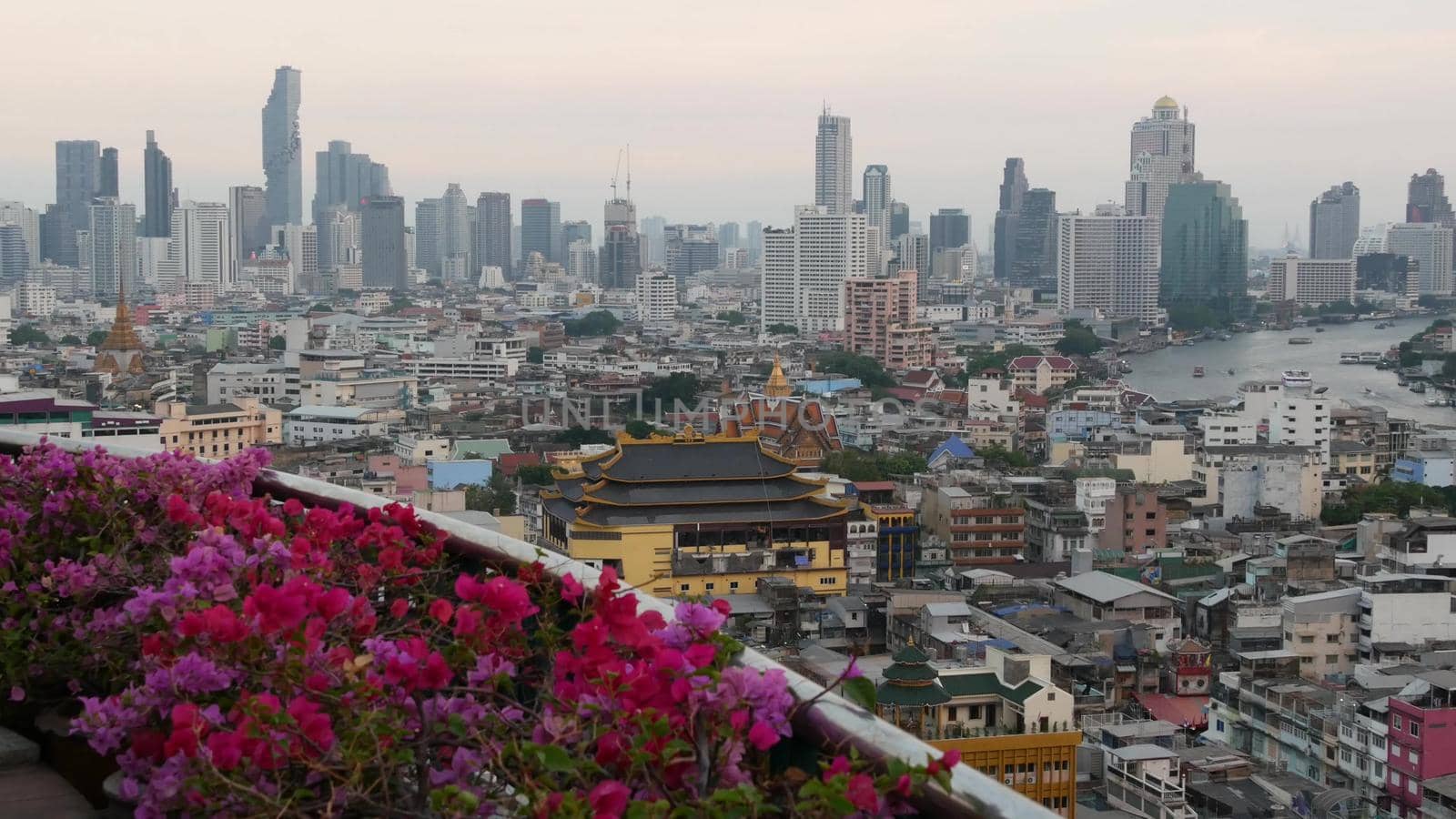 View of traditional and modern buildings of oriental city. Beautiful flowerbed against cityscape of traditional houses and skyscrapers on misty day on streets of Bangkok or Krungtep