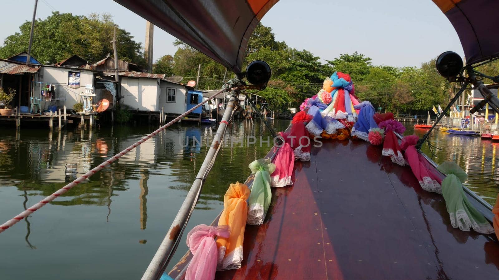 Tourist trip on Asian canal. View of calm channel and residential houses from decorated traditional Thai boat during tourist trip in Bangkok. by DogoraSun