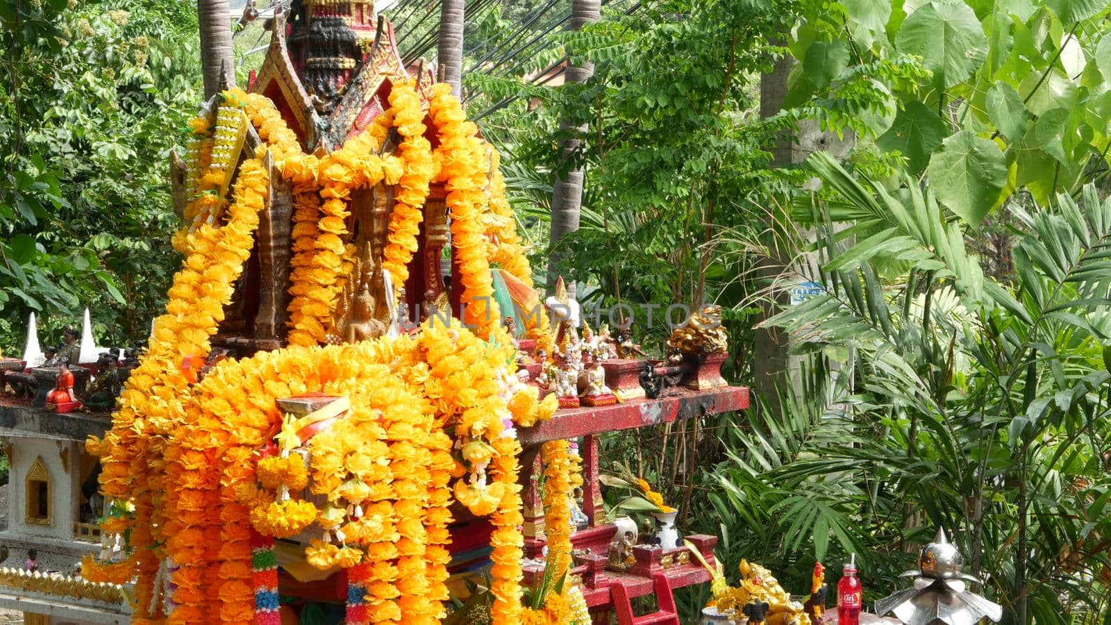 Wooden miniature guardian spirit house. Small buddhist temple shrine, colorful flower garlands. San phra phum erected to bring fortune. Traditional respect animistic rituals, pray ceremonies