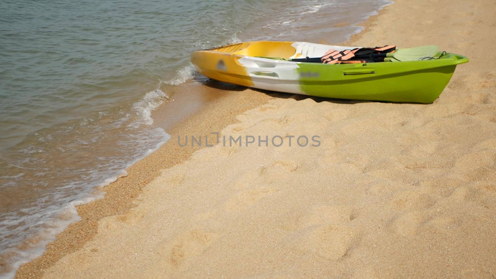 Kayak with paddles on sandy shore washed by waves of blue sea. Colorful canoe in wavy crystal water, tropical lonely island beach with copyspace. Outdoor activities, summer vacation, sport and health by DogoraSun