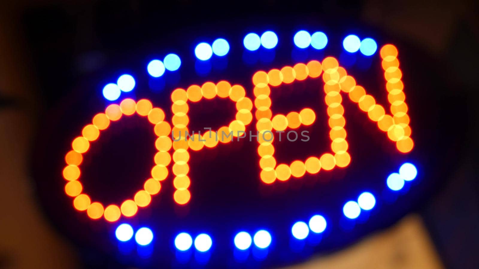 Open neon sign glowing in the dark. Vivid retro styled text at entrance on glass window. Colorful electric banner selective focus close up. Light bulbs radiance at night. Shiny illuminated lettering.