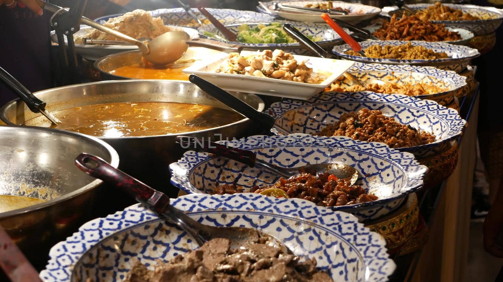 Bowls with various Asian dishes on stall. Bowls of assorted traditional Thai dishes placed on stall of street diner in evening. Oriental night market food court