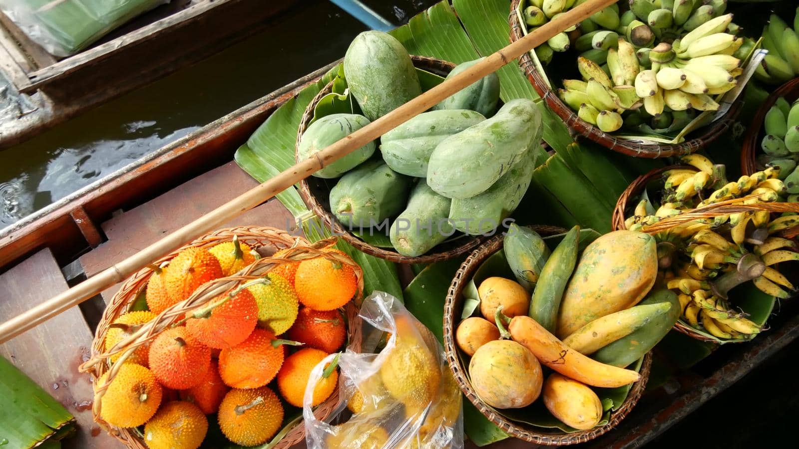 Iconic asian Lat Mayom floating market. Khlong river canal, long-tail boat with tropical exotic colorful fruits, organic locally grown vegetables. Top view of harvest and street food in wooden canoe.