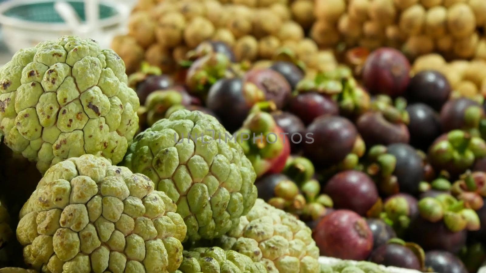 Assorted exotic fruits on stall in market. Bunch of sugar apples placed on blurred background of longans and mangosteens on stall on market in tropical country.