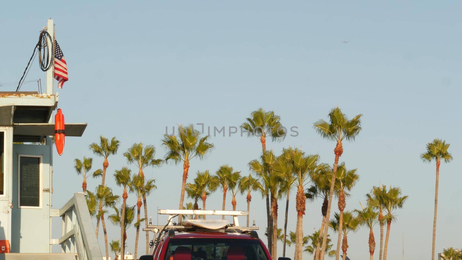 Iconic retro wooden lifeguard watch tower, baywatch red car. Life buoy, american state flag and palm trees against blue sky. Summertime california aesthetic, Santa Monica beach, Los Angeles, CA USA.