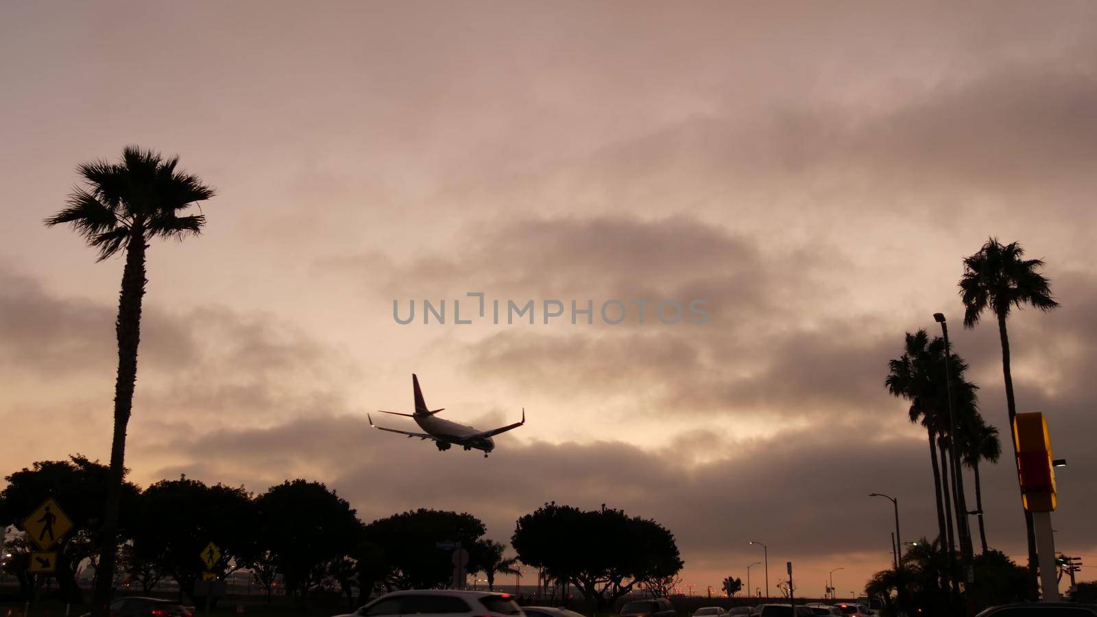 Airplane landing in LAX airport at sunset, Los Angeles, California USA. Passenger flight or cargo plane silhouette, dramatic cloudscape. Aircraft arrival to airfield. International transport flying.