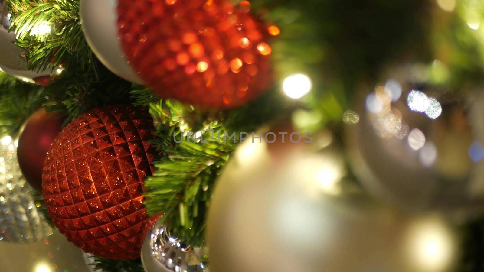 Closeup of Festively Decorated Outdoor Christmas tree with bright red balls on blurred sparkling fairy background. Defocused garland lights, Bokeh effect. Merry Christmas and Happy Holidays concept